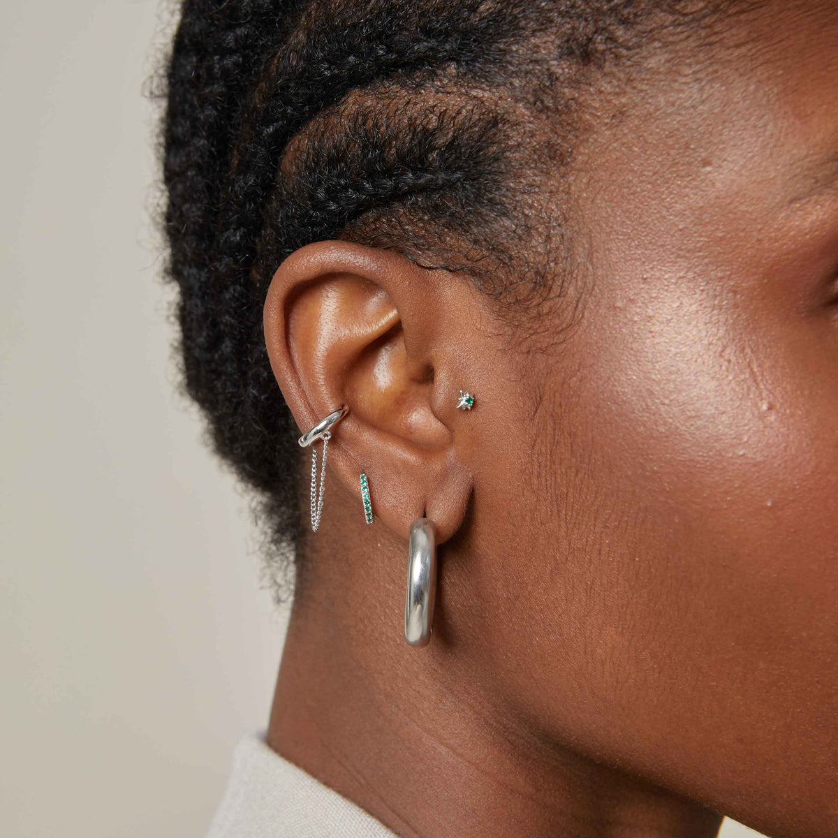 May Birthstone Huggies in Silver with Emerald CZ worn with bold silver hoops, emerald star barbell and chain ear cuff